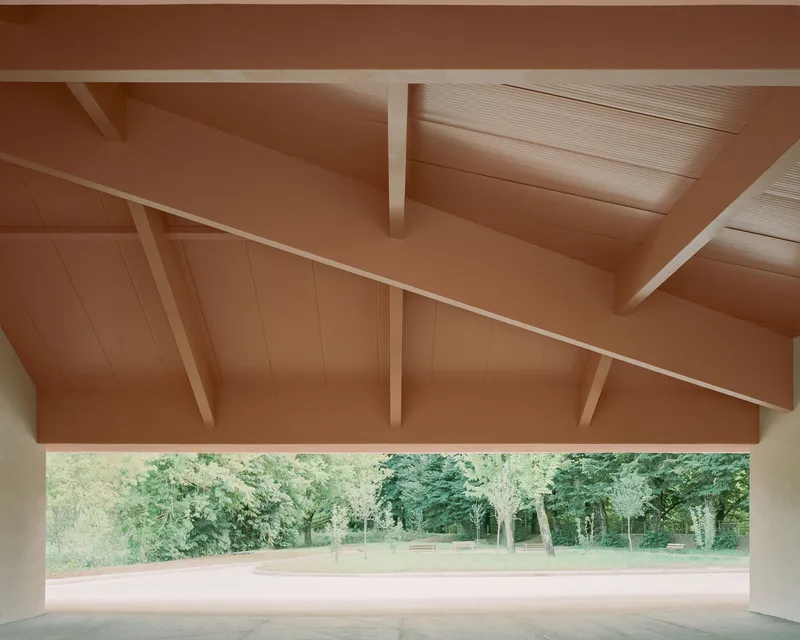 Covered porch with exposed timber beams and corrugated metal ceiling framing view of park landscape