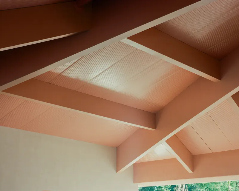 Upward view of intersecting gabled ceiling with timber beams and corrugated metal panels in warm light