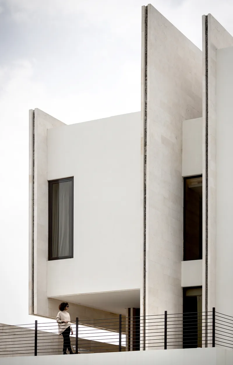 White concrete towers framing the upper terrace with horizontal railing and a person standing in afternoon light