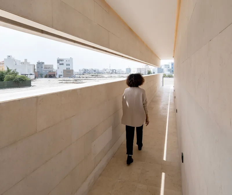 Limestone-clad corridor with horizontal window overlooking the surrounding neighborhood as a person walks toward light