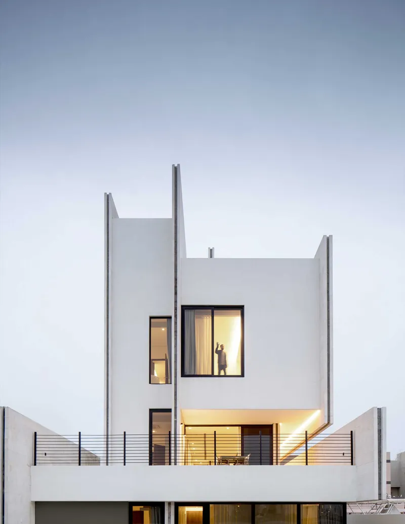 Rear facade at twilight showing illuminated windows and terrace with dining furniture behind horizontal wire railings