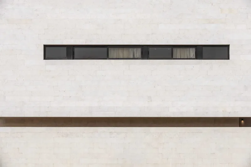 Horizontal ribbon window with six panels set into a pale travertine facade with bronze detailing below