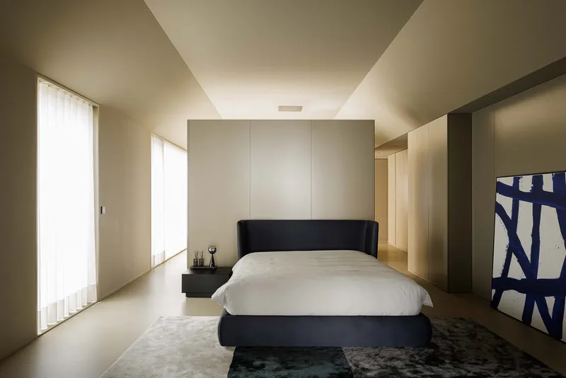 Bedroom with black upholstered bed, backlit storage wall, and filtered light from sheer curtains