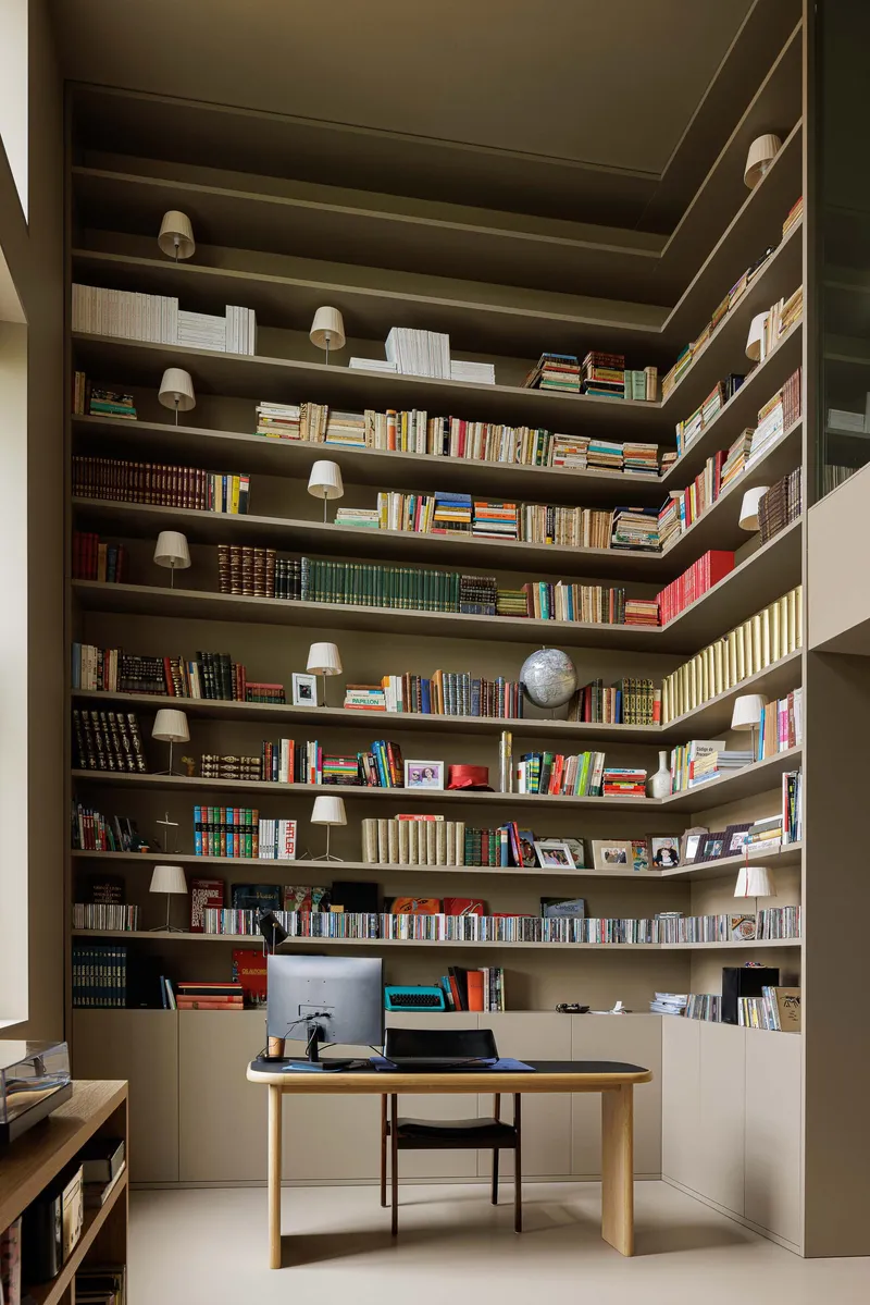 Library nook with floor-to-ceiling bookshelves wrapping corner walls and a timber desk beneath small sconces