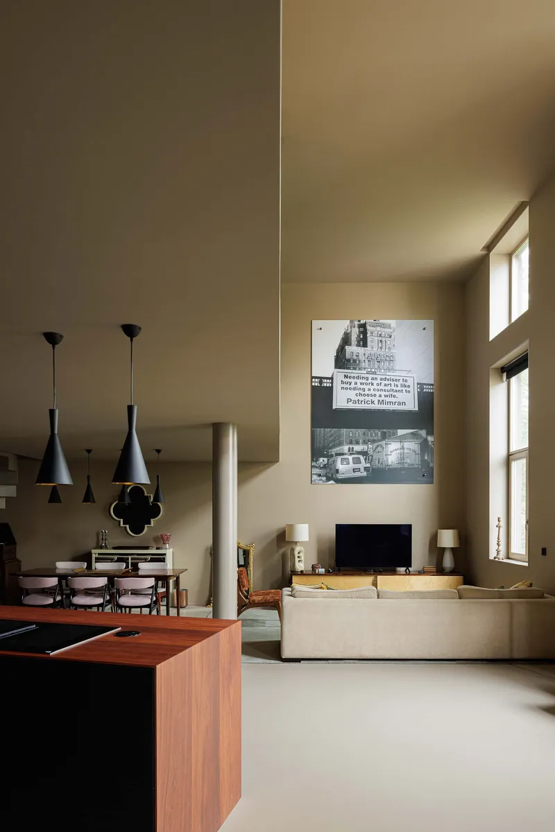 Double-height living and dining space with pendant lights and warm sunlight through high windows