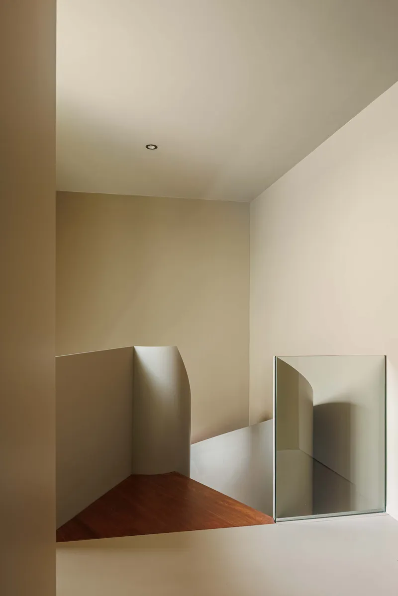 Upper-level corridor with angled walls, timber flooring, and rectangular mirror reflecting adjacent passageway