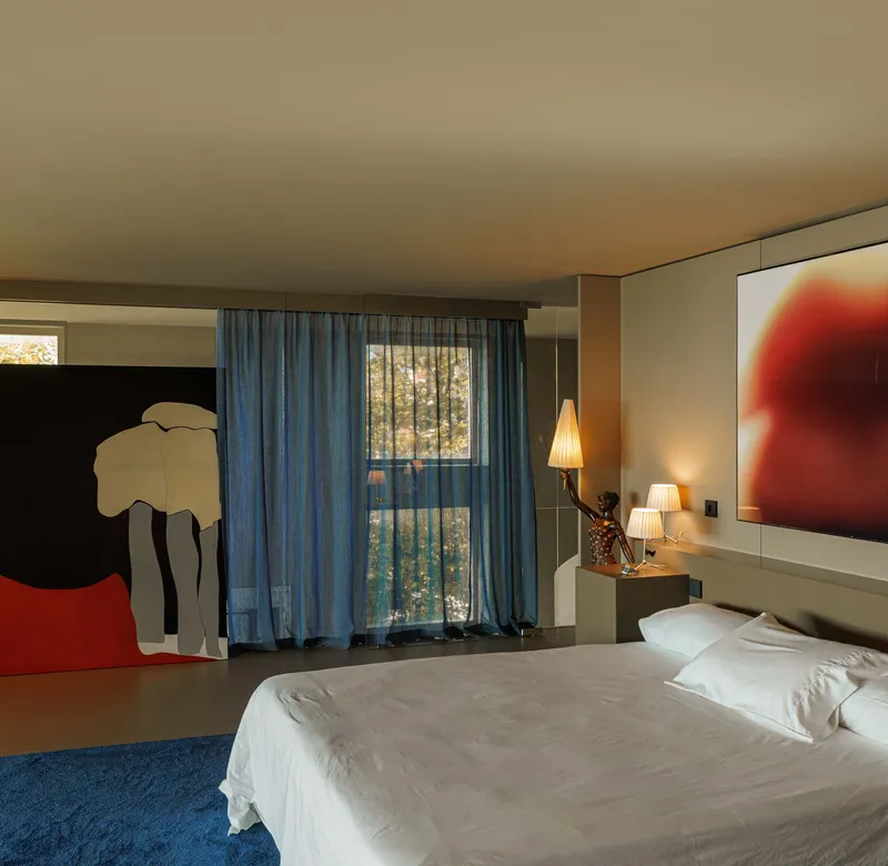 Bedroom with blue curtains, blue carpet, and large figurative paintings on opposing walls