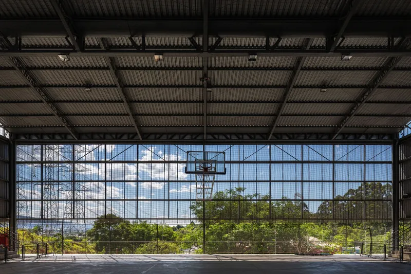 Interior sports court with exposed steel truss ceiling and full-height mesh glazing framing landscape views