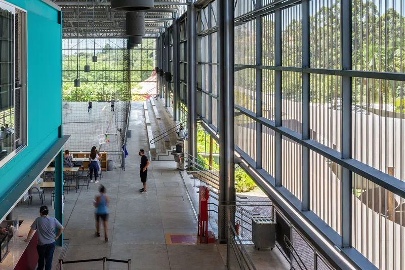 Circulation corridor along corrugated metal facade with people walking beneath exposed structural framework