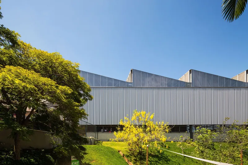 Elevated volume clad in vertical metal panels above a sloped lawn with flowering trees