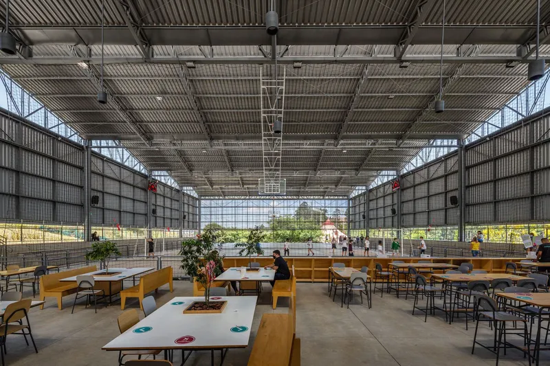 Communal seating zone with timber furniture under industrial ceiling and translucent mesh screens flanking glass walls