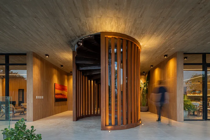 Curved timber screen wrapping cylindrical staircase beneath vaulted wood-lined ceiling with person in motion