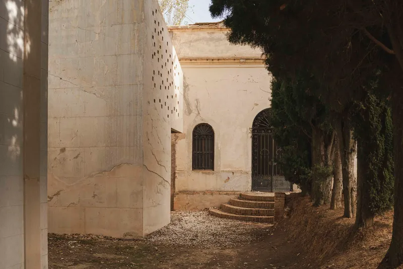 Perforated concrete tower beside stone steps leading to arched doorways framed by tall trees