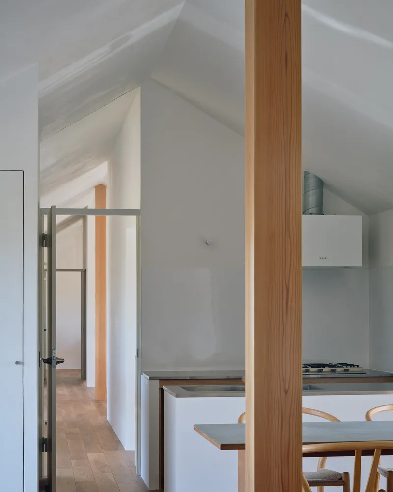 Kitchen and dining area with white cabinetry under a vaulted ceiling and timber column in soft daylight