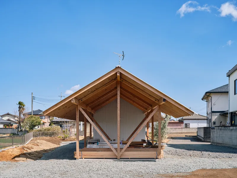 Exposed timber frame pavilion with diagonal bracing and corrugated metal walls on gravel site