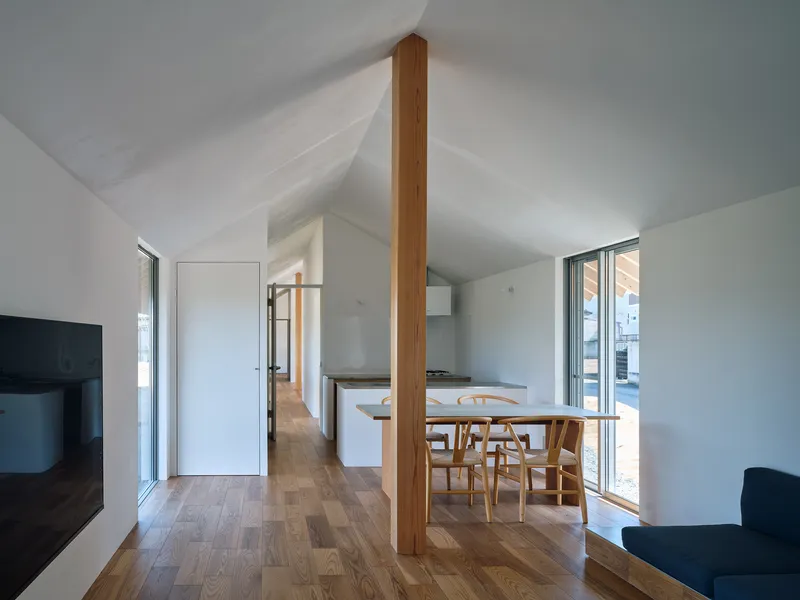 Open plan dining area with central timber column under white gabled ceiling and timber flooring