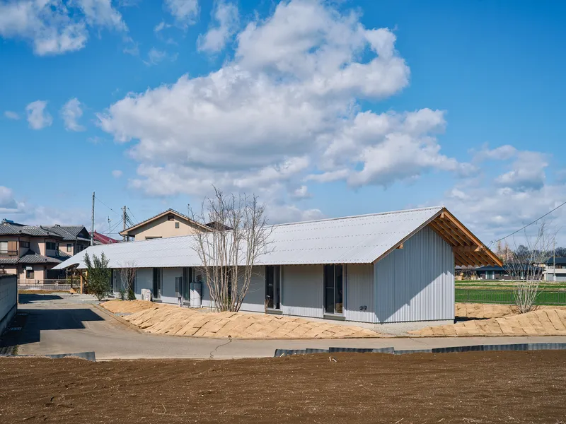 Street view of the corrugated metal volume with gabled roof and timber eaves in a neighborhood setting