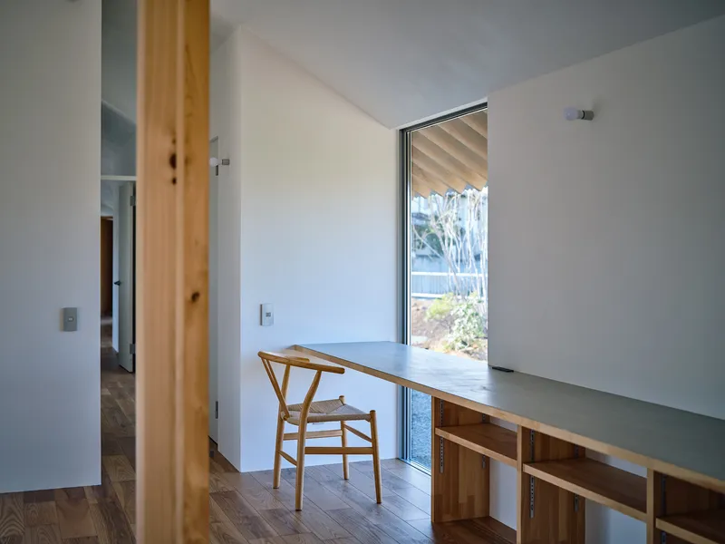 Built-in desk with timber shelving below a tall window framing views of shrubs and trees