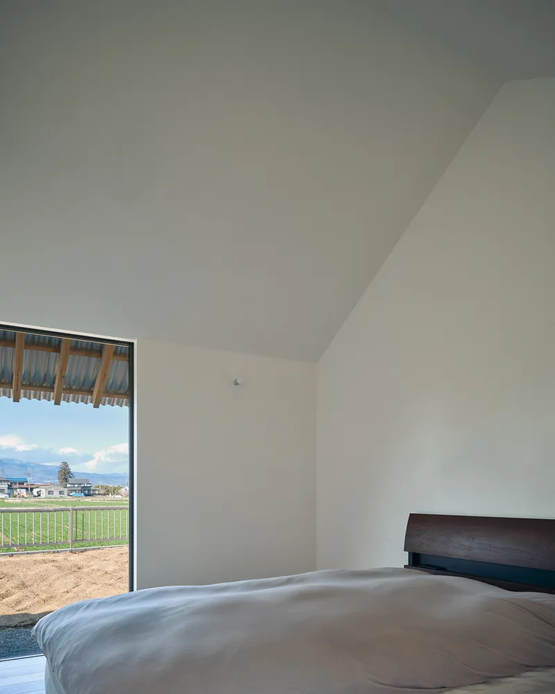 Bedroom with sloped white ceiling and glazed door opening to green fields under cloudy skies