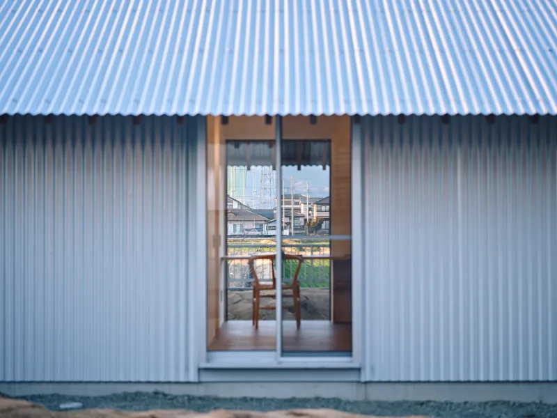 Corrugated metal facade with timber-framed glazed door reflecting the rural neighborhood at dusk