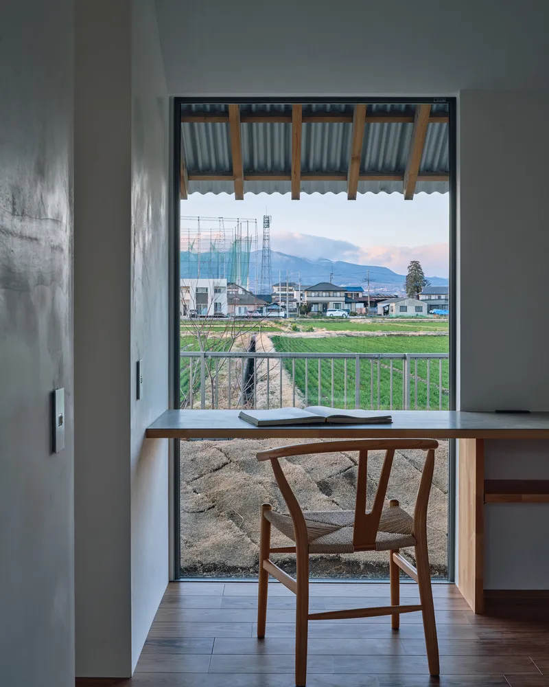 Framed view through a full-height window of rice fields and distant mountains at dusk