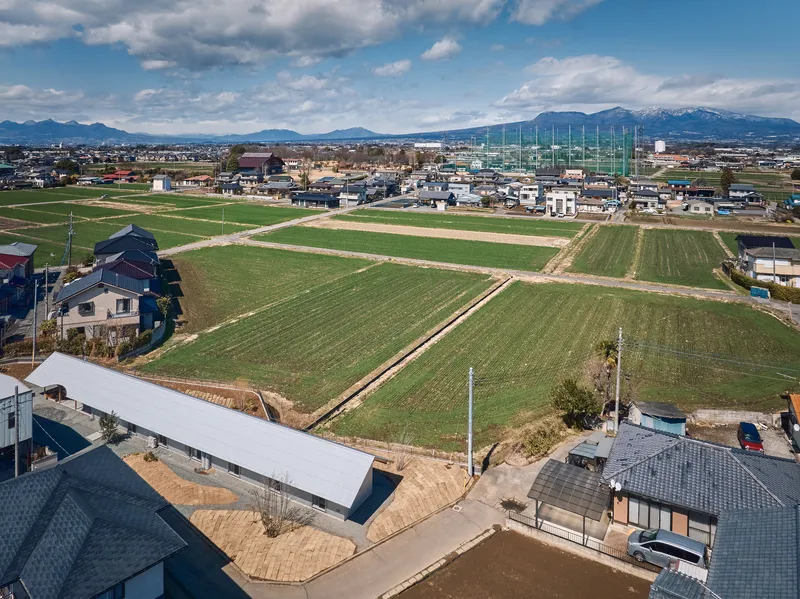 Aerial view of a white gabled roof structure bordered by agricultural fields and neighboring houses