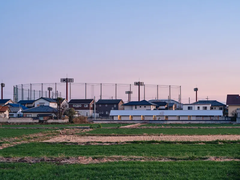 Distant view of the white horizontal volume across green fields at twilight with netting structures beyond