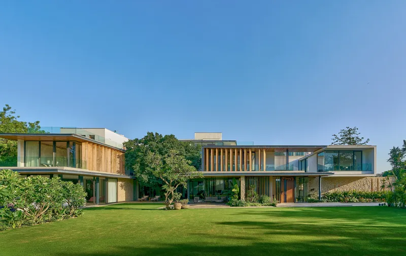 Garden view of the three-volume composition with timber cladding and glass facades under a clear blue sky