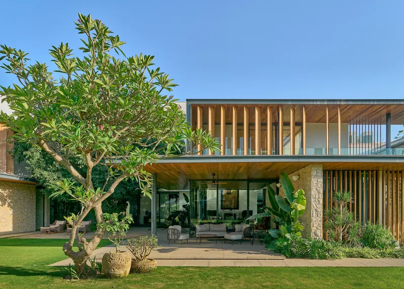 Cantilevered upper volume with vertical timber louvers above the glass-enclosed ground floor terrace with potted trees