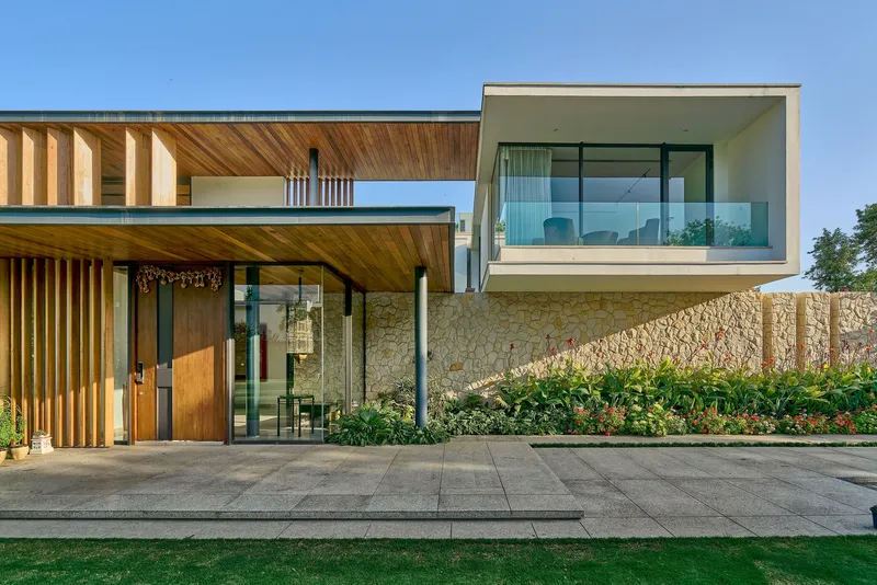 Entry facade showing cantilevered glazed volume over textured stone wall with planted bed below