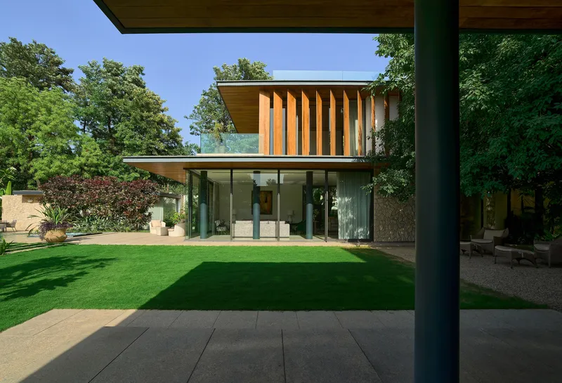 Covered terrace with black steel column overlooking lawn and glazed facade with vertical timber louvers above