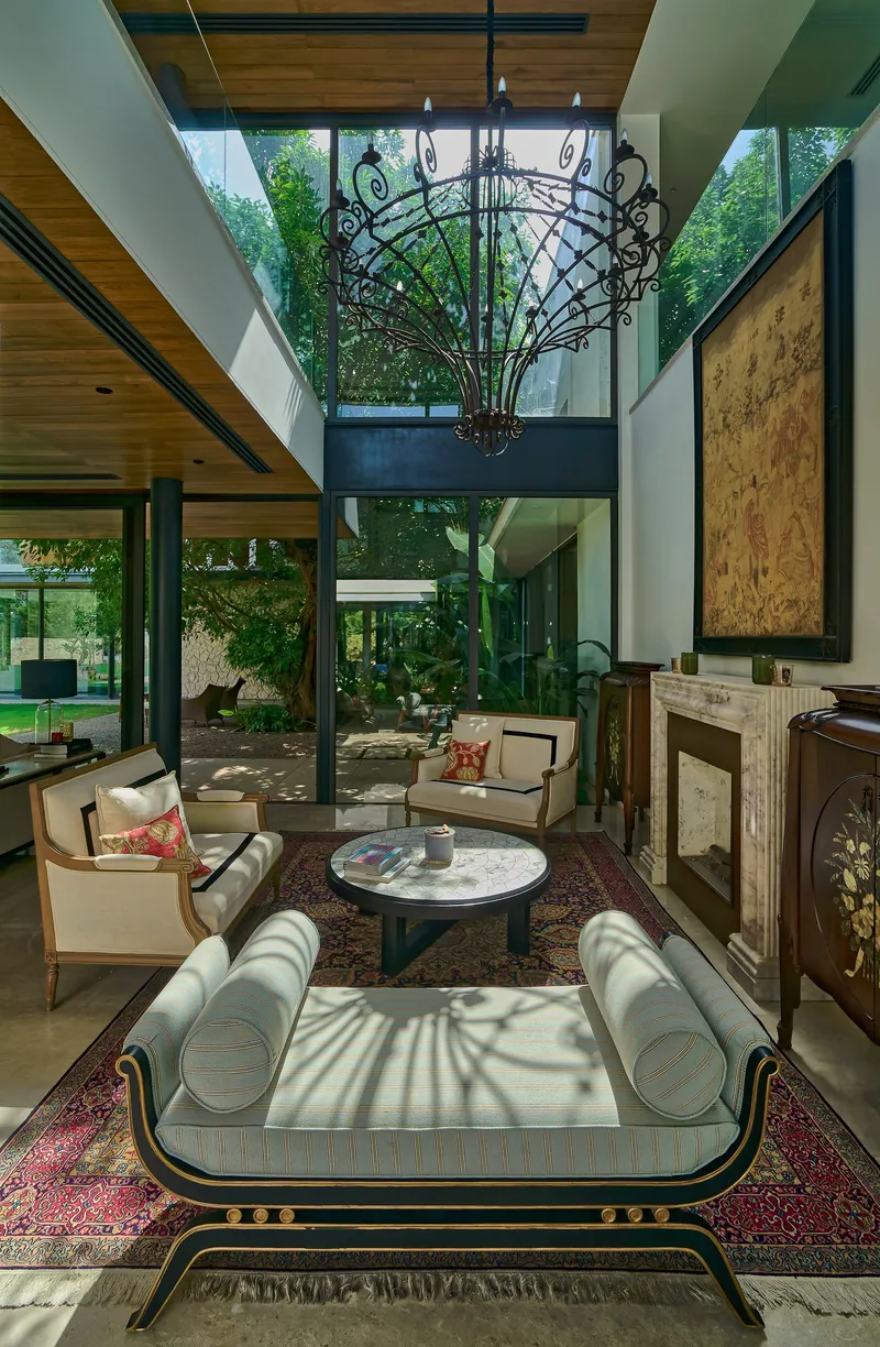 Double-height living room with ornamental metal chandelier suspended above seating and glass walls overlooking garden