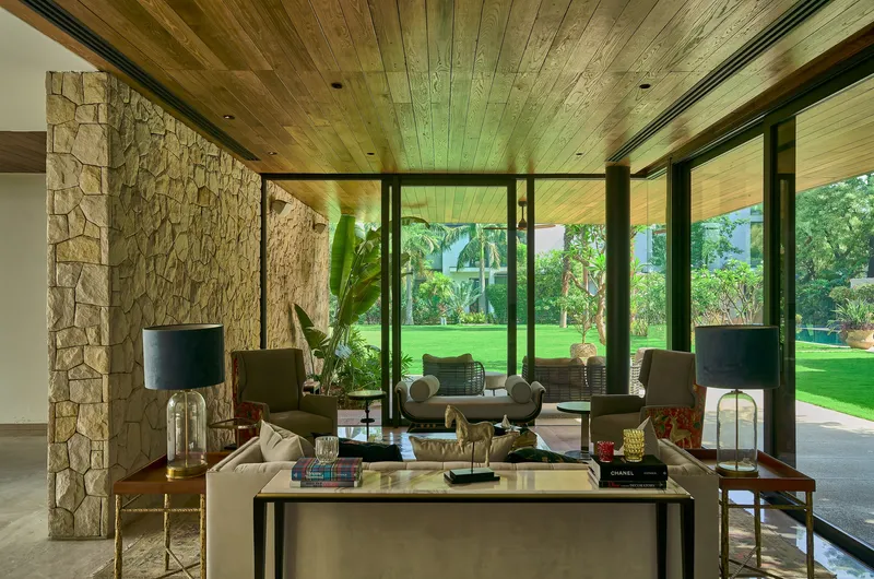 Living room with stone veneer columns, timber plank ceiling and floor-to-ceiling glass opening to lawn