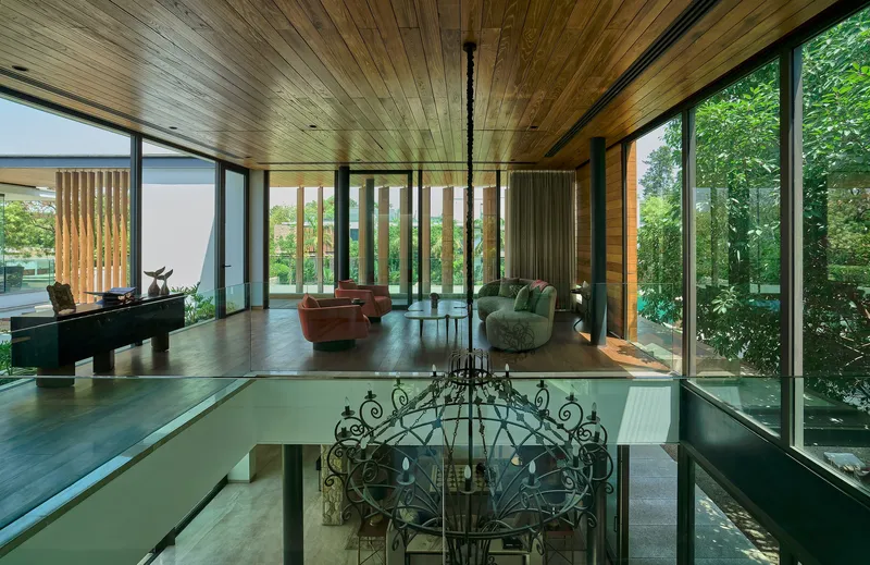 Double-height interior space with timber ceiling, wrought-iron chandelier and glazed walls framing garden views