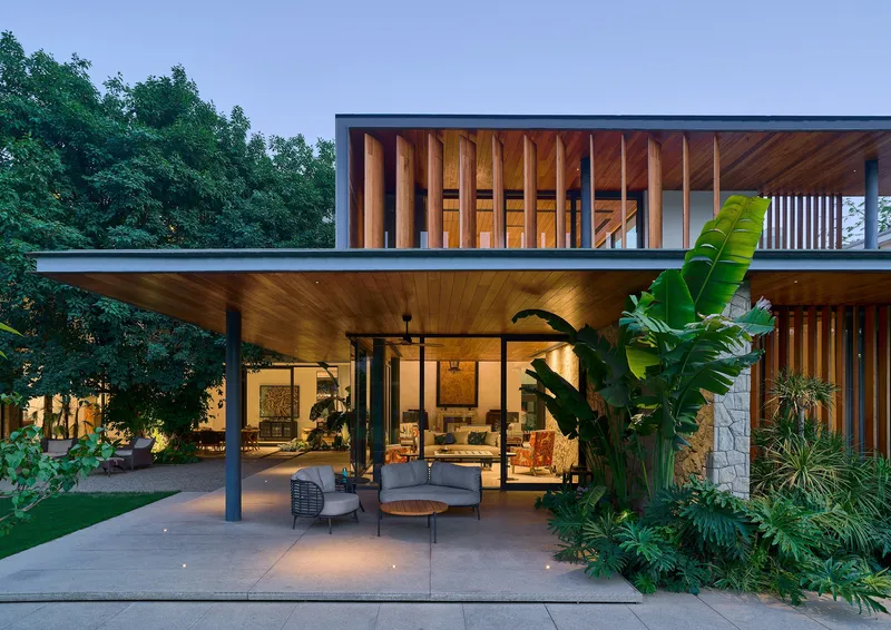 Two-story facade at dusk with timber cladding, vertical louvres and cantilever overhang sheltering terrace below