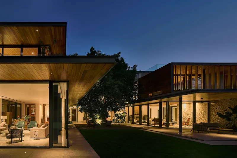 Courtyard view at twilight showing two wings with timber ceilings and lit stone wall between
