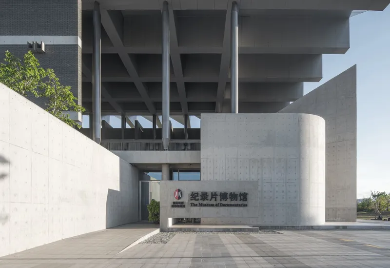 Entrance plaza with cylindrical concrete volume and exposed waffle slab structure above under clear skies