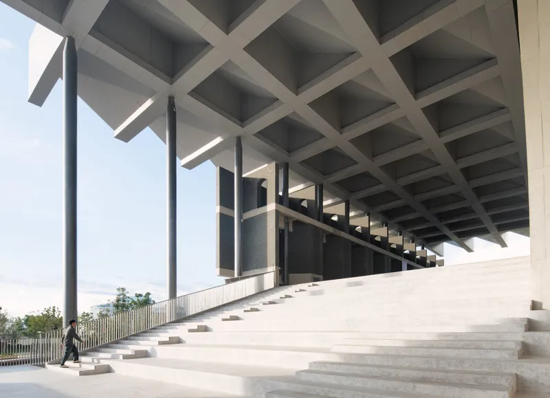 Wide ceremonial staircase beneath a coffered concrete ceiling with a lone figure walking at the base