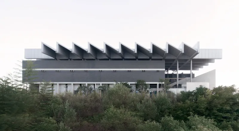 Lateral view of the elevated structure with sawtooth roof profile rising above dense surrounding vegetation