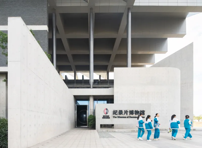 Courtyard entrance with cylindrical concrete element and group of uniformed visitors walking across the paving