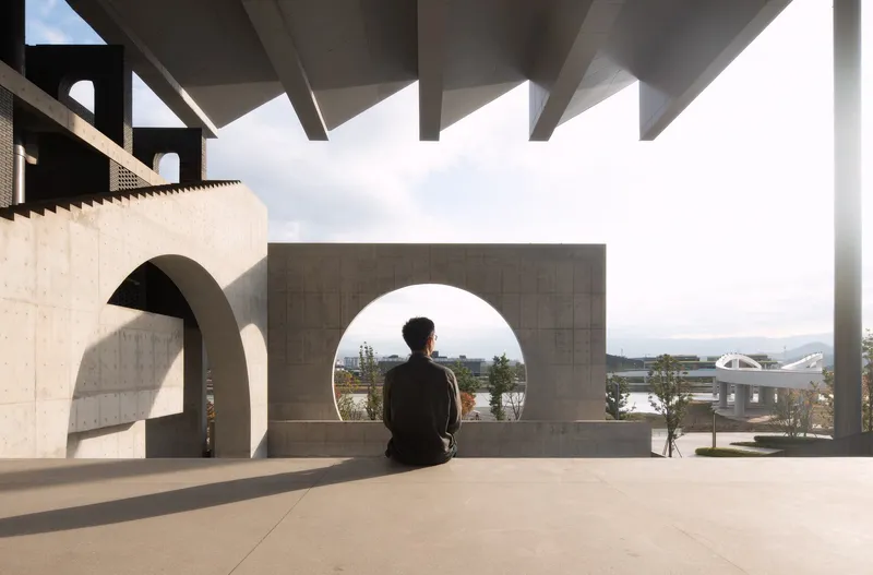 Visitor seated on a concrete bench beneath a coffered canopy looking through a circular opening