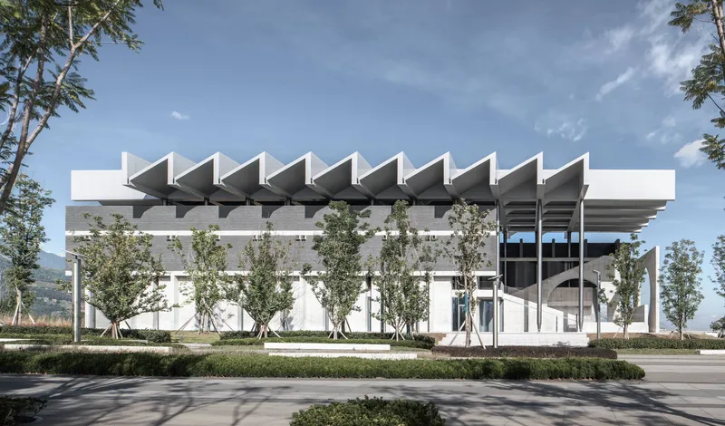 Side facade with repeating angular concrete canopy elements above young planted trees and lawn