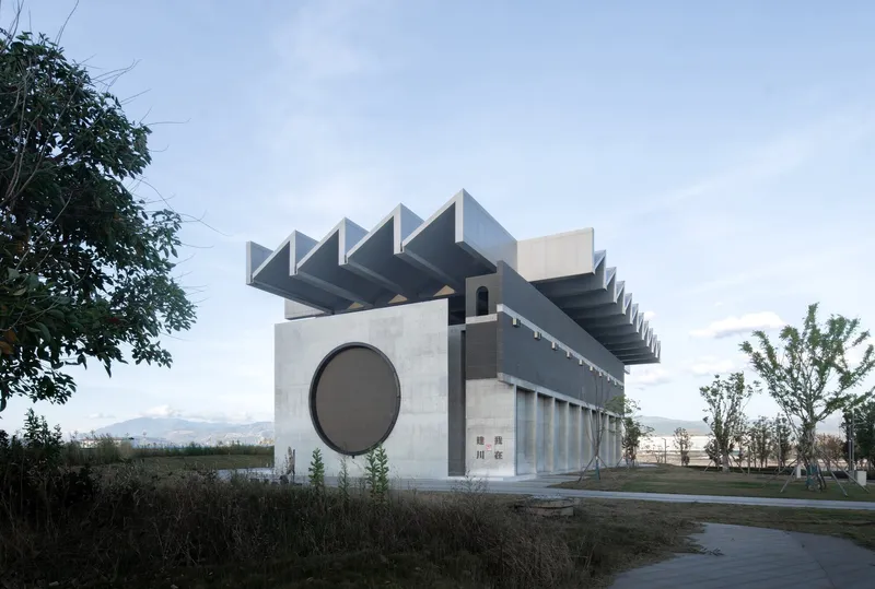 Side view showing the folded roof canopy and circular window in concrete facade at dusk