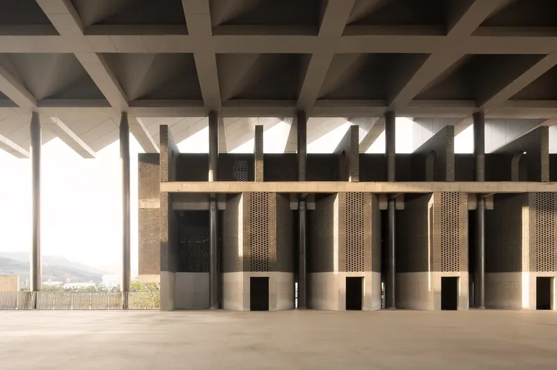 Interior row of perforated bronze cylindrical columns beneath a coffered concrete ceiling
