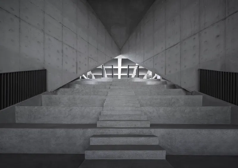 Central concrete staircase rising between board-formed walls toward a backlit arched opening