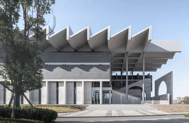 Front elevation showing folded concrete roof forms and arched openings framed by mature trees