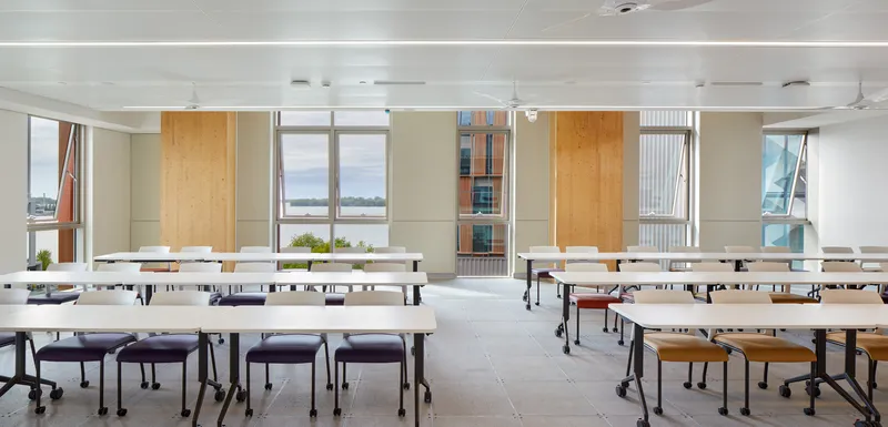 Classroom interior with movable white tables arranged in rows beneath linear ceiling lights and operable windows
