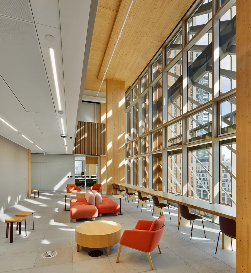 Interior lounge space with floor-to-ceiling glazed wall and timber framing in afternoon sunlight