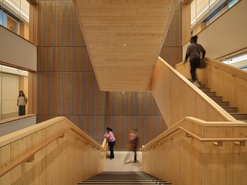 View down the timber-clad stairwell with vertical slatted wall as people ascend and descend