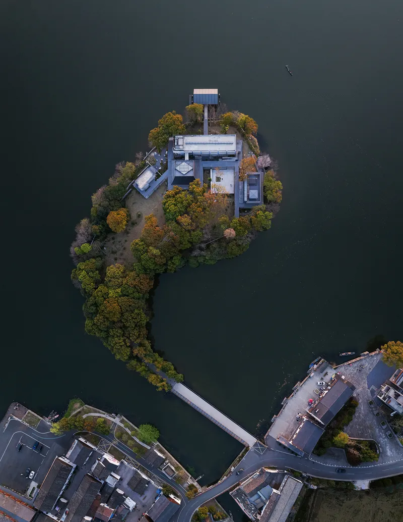 Aerial view of the pavilion on a small forested island connected by footbridge in autumn